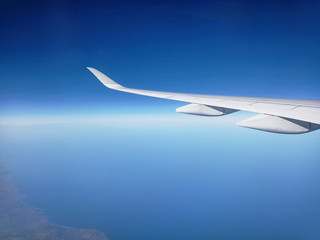 Wing of airplane over white clouds viewed from window - Aircraft flying on blue sky with copy space above and below.
