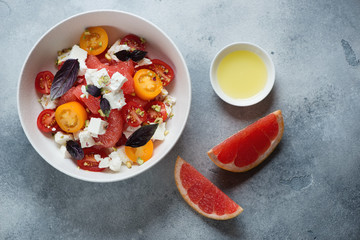 Bowl of grapefruit, feta cheese and cherry tomatoes salad, above view on a light-blue stone background, horizontal shot with space