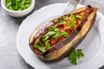 Whole eggplant stuffed with vegetables on white plate on grey background . Imam bayildi, Turkish cuisine.