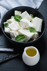 Black bowl with feta cheese, fresh spinach leaves and olive oil, vertical shot, close-up