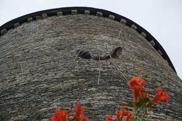 old stone wall with flowers and metal sculpture on a tower