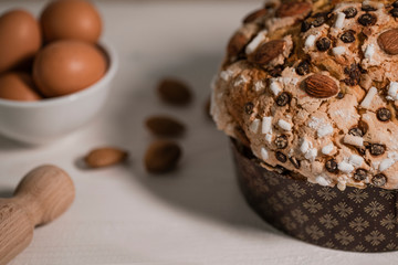 Panettone, typical Italian Christmas cake with chocolate and almonds. In the background the ingredients used to make panettone, eggs, flour, chocolate.
