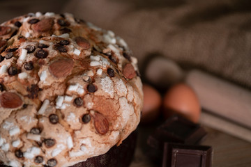 Panettone, typical Italian Christmas cake with chocolate and almonds. In the background the ingredients used to make panettone, eggs, flour, chocolate.
