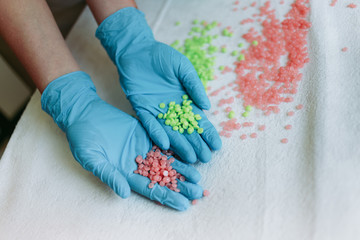 Closeup of gloved hands holding pink and green granules of depilatory wax.