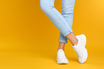 Woman wearing stylish sneakers on yellow background, closeup. Space for text