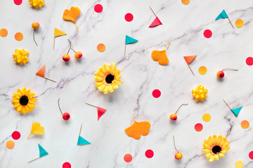 Autumn gingko leaves, paper confetti and toothpick flags. Flat lay on white marble table. Abstract Fall seasonal background with yellow flowers,