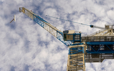 Majestic construction crane raises against the blue cloudy sky.