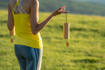 Attractive Caucasian woman holding Koshi chimes musical instruments in her hands, enjoying the healing and relaxing sounds of the bells on a sunny morning in the heart of nature.