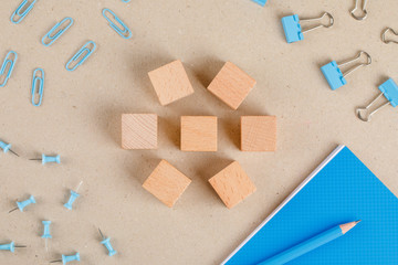 Office supplies concept with wooden cubes, paper and binder clips, pencil, notebook, push pins on paper background flat lay.