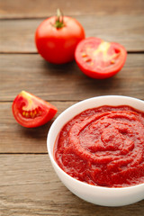 Tomato ketchup sauce in a bowl with tomatoes on grey background. Vertical foto