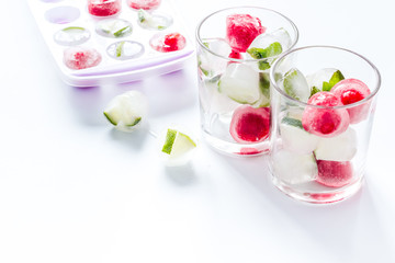 Cocktail glasses with berries in ice cubes on white table
