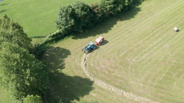 Aerial view of blue tractor with round baler discharging a fresh hay bale during harvesting