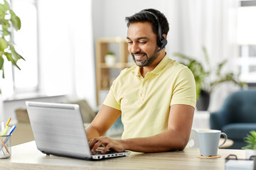 remote job, technology and people concept - happy smiling indian man with headset and laptop computer having conference call at home office