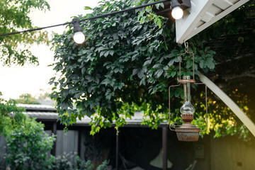 Antique vintage iron lantern hangs on the terrace of the house against the backdrop of greenery in the evening.