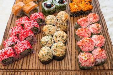 Different types of delicious and juicy sushi and rolls on a wooden board