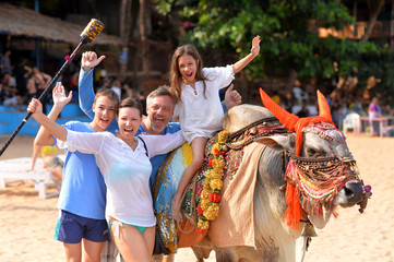 Cute little girl in white dress sitting on bull, family standing nearby