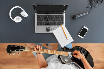 leisure, music and people concept - young man or musician with laptop computer playing guitar...