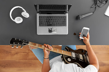 leisure, music and people concept - young man or musician with guitar, smartphone and laptop...