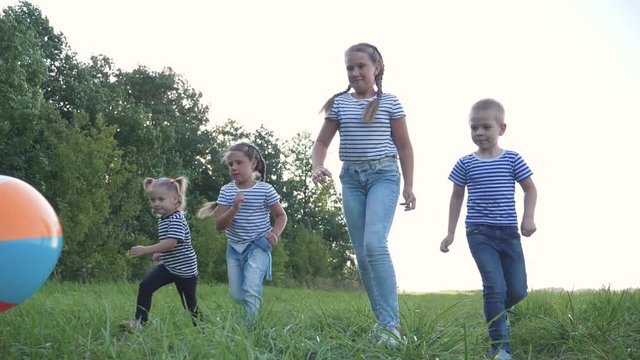 Happy Family Of Children Has Fun In The Park. Children With A Crowd Run For A Colorful Ball, Catching Up. Kids At Sunset In The Park Have Fun Playing. Team Game Girls And Boy.