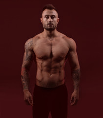 Fototapeta premium Bodybuilder strong man with an ideal body on red dark background.