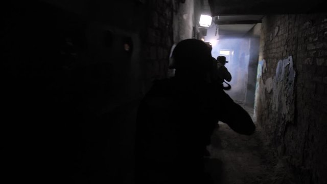 Back view of armed military men following the chain while walking through darkness and smoke of ruined building. Special forces unit conducting anti-terrorist action inside captured by enemy territory