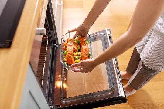 Culinary, Food And People Concept - Woman Cooking Salmon Fish With Vegetables In Baking Dish In Oven At Home Kitchen