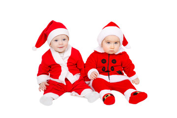 Two adorable young babies are sitting in santa claus suit and hat