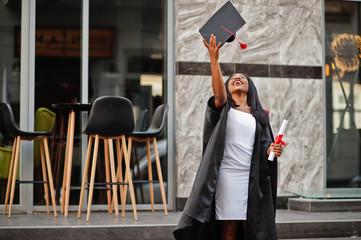 Young female african american student with diploma poses outdoors.