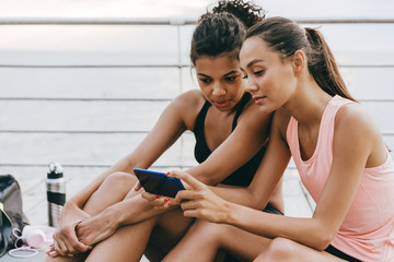 Image of sportswomen using cellphone while sitting on promenade