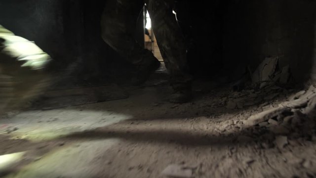 Close-up of soldiers' lower body in camouflage pants and ankle boots during capture of enemy-occupied building. Squad of special forces army males in uniform invading building captured by terrorists