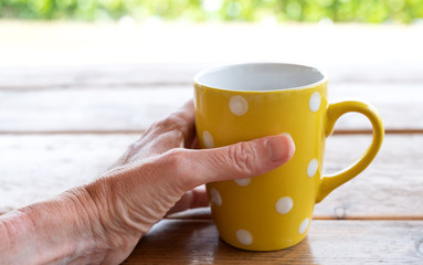 Female hand holding yellow polka dot mug outdoors
