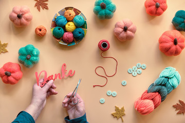 Hands with scissors cutting out word Danke from paper. It means Thank you in German language. Hobby craft materials in Fall colors. Autumn background with felt pumpkins, wool bundle, buttons.