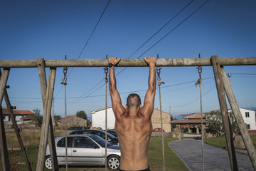 Young muscular man performing pull ups in a wooden swing with a clear blue sky in summer. Asturias,...