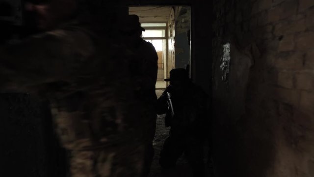 Diverse special forces unit clearing dark floor of captured by enemy ruined building, following the chain and leaving fighter to cover. Accurate teamwork of professional army males on assault mission