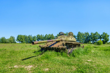 Fototapeta na wymiar Remains of former battle tank are rusting in green field. Summer weather, no one around