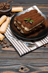 Classic tiramisu dessert on ceramic plate on wooden background