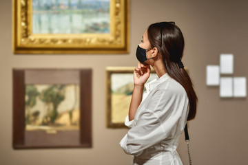 Woman visitor wearing an antivirus mask in the historical museum looking at pictures.