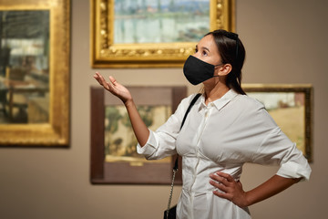 Woman visitor wearing an antivirus mask in the historical museum looking at pictures.