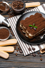 Classic tiramisu dessert and savoiardi cookies on ceramic plate on wooden background