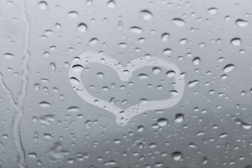Drawn heart on the transparent window with raindrops on it. Blurred background. Love theme. Calm mood.