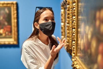 Woman visitor wearing an antivirus mask in the historical museum looking at pictures.
