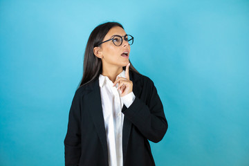 Young beautiful business woman over isolated blue background surprised with hand on head for...