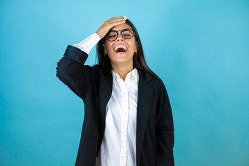 Young beautiful business woman over isolated blue background putting one hand on her head smiling...
