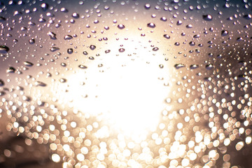 Raindrops on cars window with the yellow sun light in the middle and purple shades at the very top....