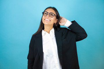 Young beautiful business woman over isolated blue background relaxing and stretching, arms and hands behind head and neck smiling happy