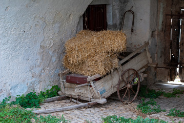 Old broken cart with hay and a red suitcase