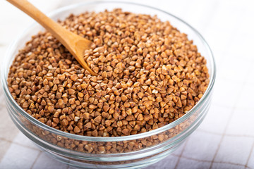 Bowl of raw buckwheat with spoon on wooden background. Buckwheat groats (hulled seeds) in bowl.