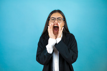 Young beautiful business woman over isolated blue background shouting and screaming loud to side with hands on mouth