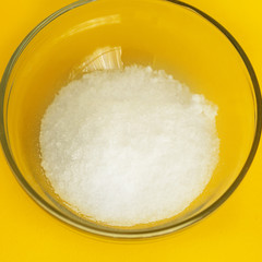 Salt in a glass bowl on a yellow square background close up.