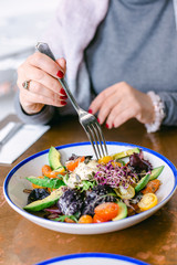 Happy woman eating healthy salad with tomatos cherry,  greens, avocado and carrots. Woman wearing grey jersey is eating business lunch